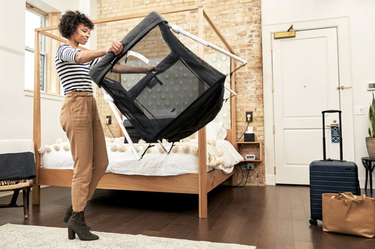 Photograph of a woman opening the Guava Family Lotus Travel Crib in a hotel room.